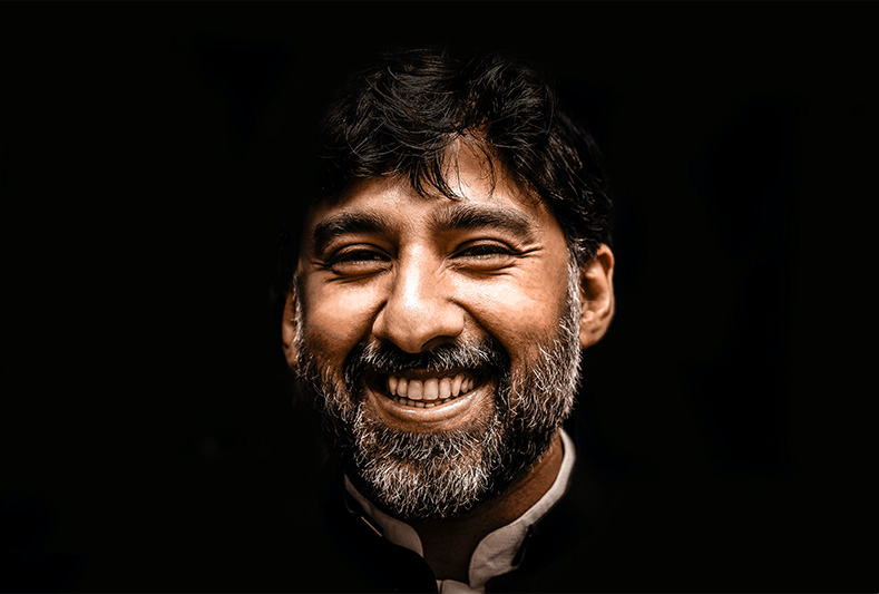 WELL SAID: TORONTO SPEECH THERAPY. A man with dark hair and a beard smiles broadly against a black background, his face warmly lit and showing a sense of happiness and friendliness.