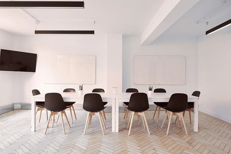 WELL SAID: TORONTO SPEECH THERAPY. A modern conference room with a long white table surrounded by black chairs, two whiteboards on the wall, small potted plants on the table, a wall-mounted TV, and light herringbone-patterned flooring.