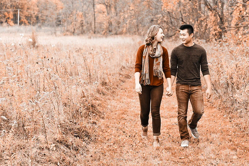 WELL SAID: TORONTO SPEECH THERAPY. A smiling couple walks hand in hand down a grassy path through a field with autumn foliage, dressed in cozy fall clothing.