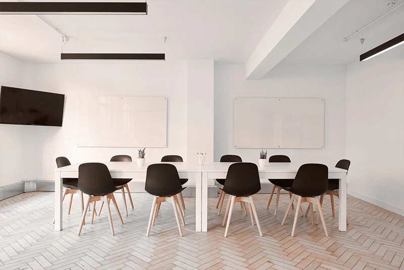 WELL SAID: TORONTO SPEECH THERAPY. A modern conference room with a white table, eight black chairs, two whiteboards on the wall, a mounted flat-screen TV, and minimalist decor featuring small plants on the table.