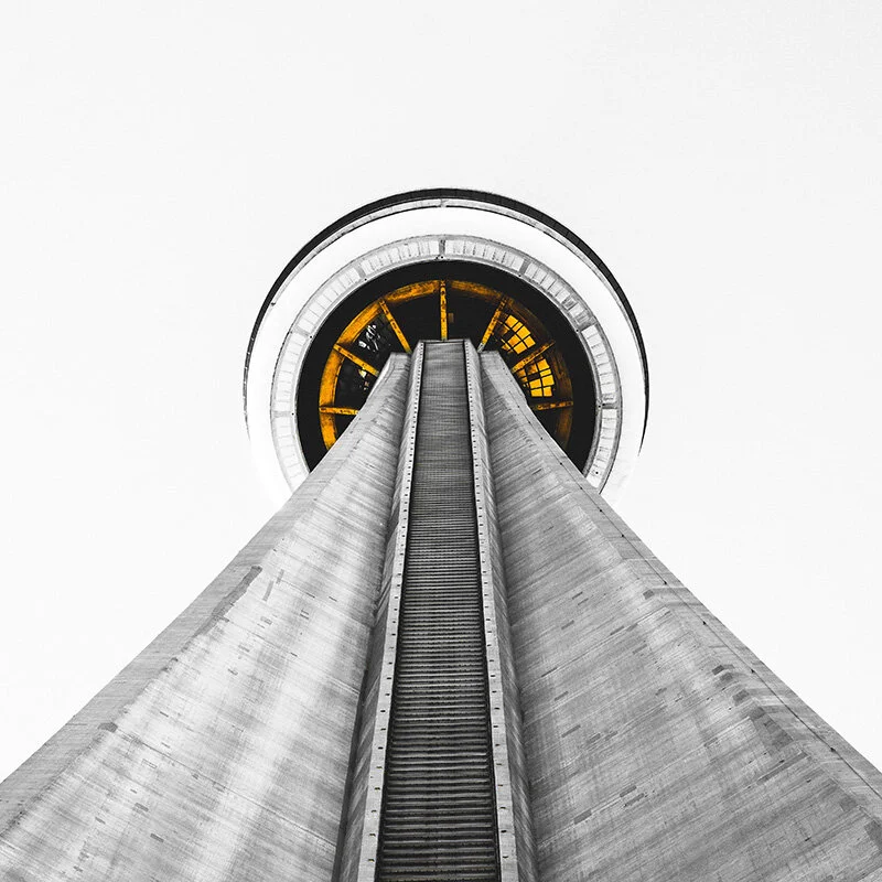 WELL SAID: TORONTO SPEECH THERAPY. A dramatic upward view of a tall concrete observation tower with a circular top, featuring a yellow-lit ring inside, set against a plain white sky.