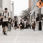 WELL SAID: TORONTO SPEECH THERAPY. A group of people walk along a city street, some looking at their phones or cameras. A pedestrian crossing sign is visible on the right, and buildings line both sides of the street.