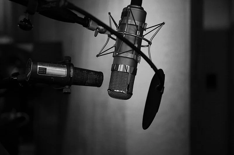 WELL SAID: TORONTO SPEECH THERAPY. A black and white photo of two microphones and a round pop filter set up in a recording studio, with blurred background elements.