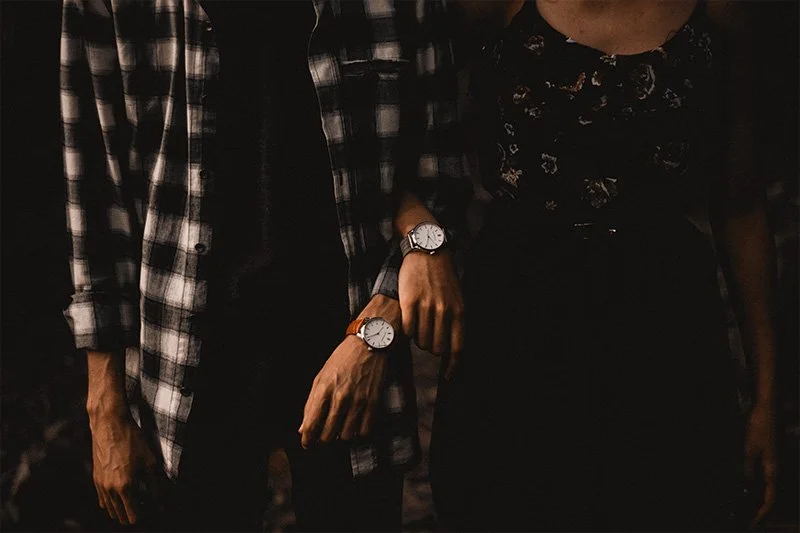WELL SAID: TORONTO SPEECH THERAPY. A couple stands side by side, their arms intertwined. Both wear watches; one person wears a plaid shirt and the other a floral dress. The image is moody and dimly lit, highlighting their clasped hands and wrists.