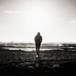 WELL SAID: TORONTO SPEECH THERAPY. A person walks alone on a rocky Toronto shore toward the ocean, silhouetted against the bright sun low in the sky, creating a dramatic, high-contrast scene.