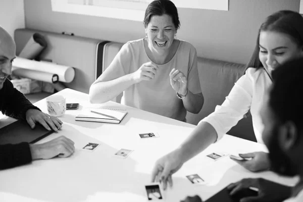 WELL SAID: TORONTO SPEECH THERAPY. Four people sit around a table in Toronto, smiling and interacting with small photos spread out in front of them. One woman laughs while another reaches toward the center. Notebooks and a coffee mug are also on the table.