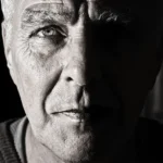 WELL SAID: TORONTO SPEECH THERAPY. A close-up black and white photo of an older man’s face, showing deep wrinkles and intense expression. Shot in Ontario, half his face is brightly lit while the other half is in shadow, highlighting strong contrast. Suitable for adults.