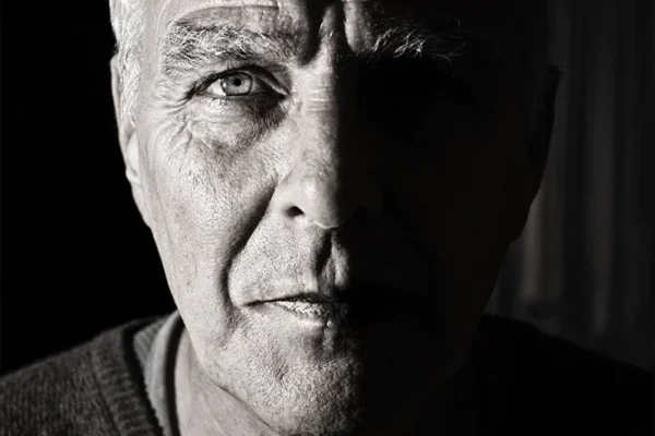 WELL SAID: TORONTO SPEECH THERAPY. A close-up black and white photo of an older man’s face, showing deep wrinkles and intense expression. Shot in Ontario, half his face is brightly lit while the other half is in shadow, highlighting strong contrast. Suitable for adults.