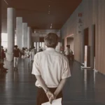 WELL SAID: TORONTO SPEECH THERAPY. A person stands indoors with their back to the camera, holding a paper behind their back, in a spacious Toronto corridor with other adults walking and sitting in the background.