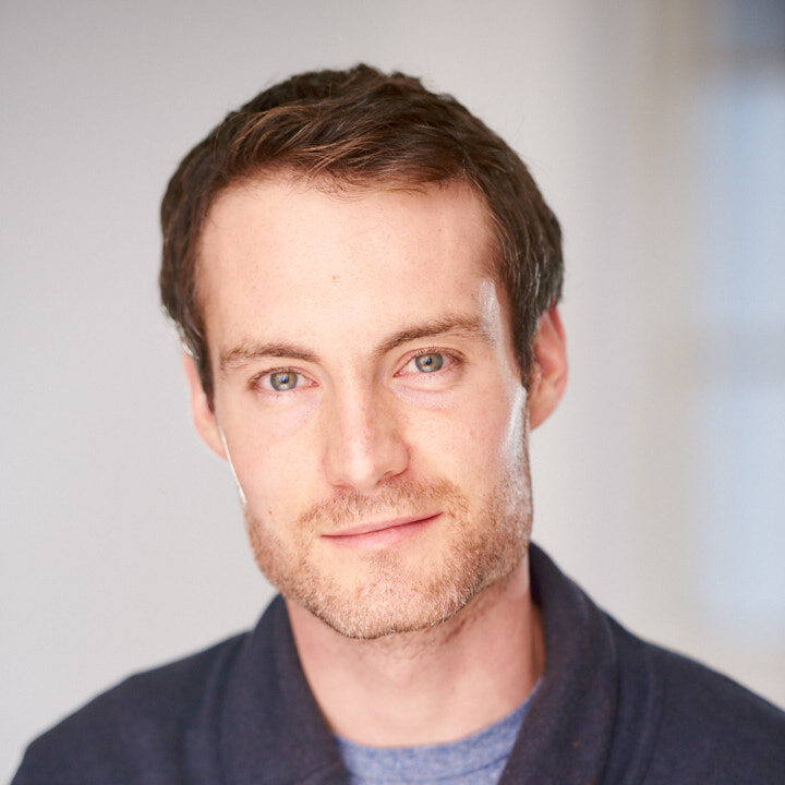 WELL SAID: TORONTO SPEECH THERAPY. A man with short brown hair and light eyes is looking at the camera with a slight smile. He is wearing a blue shirt and a dark jacket. The softly blurred, light-colored background suggests an Ontario setting.