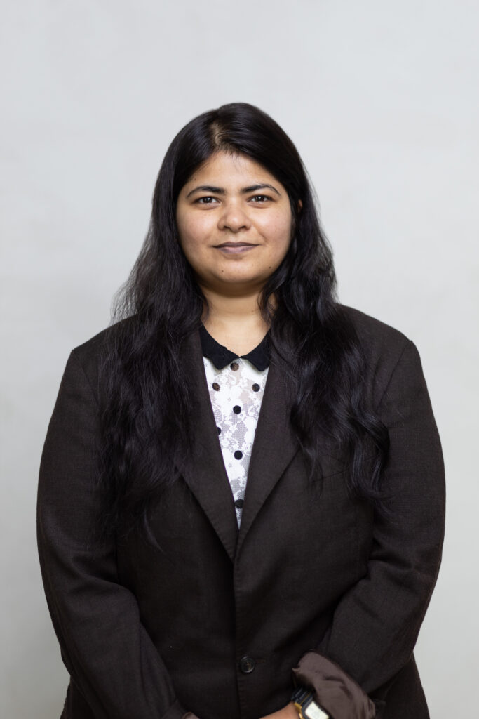 WELL SAID: TORONTO SPEECH THERAPY. A woman with long black hair wearing a black blazer over a white shirt with black polka dots stands against a plain light gray background, looking at the camera with a neutral expression, reflecting professionalism in Ontario’s speech-language pathology field.