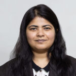 WS-0432web WELL SAID: TORONTO SPEECH THERAPY. A woman with long black hair and a neutral expression faces the camera. She is wearing a dark blazer over a light-colored top. The background is plain and light gray.